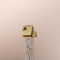Bague poison moderne en or avec pierre précieuse violette sur présentoir minimaliste en pierre poreuse beige