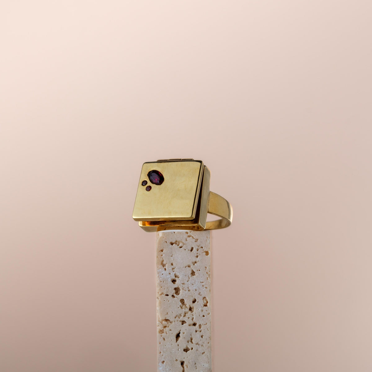 Bague poison moderne en or avec pierre précieuse violette sur présentoir minimaliste en pierre poreuse beige