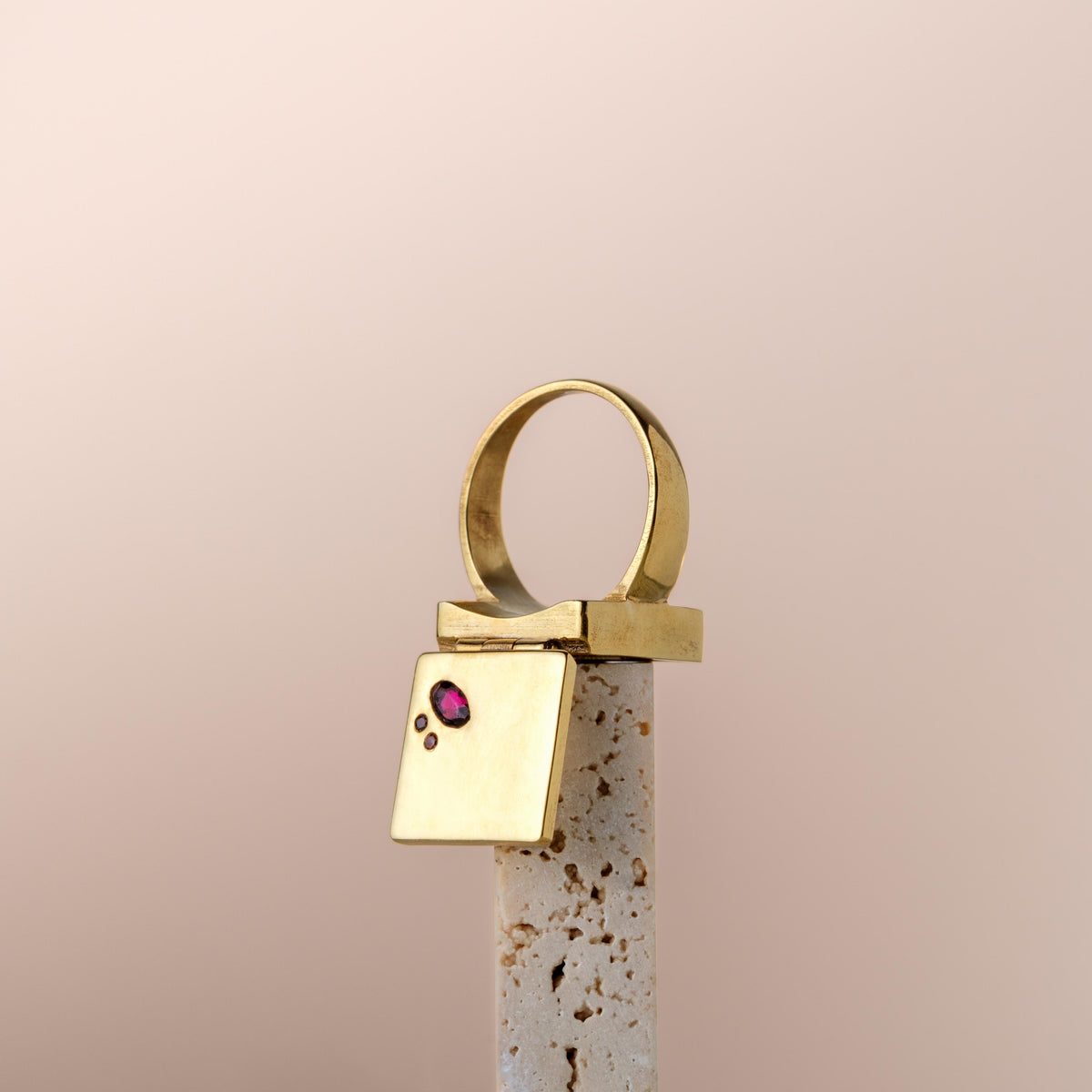 Bague poison dorée design contemporain avec pierre rose et détails géométriques sur support minéral